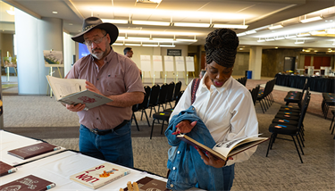 A man in a cowboy hat and a woman looking at old high school yearbooks