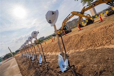 Artistic view of the shovels lined up with hardhats and backhoes behind them